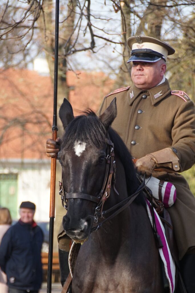 Żołnierz trzymający w ręku chorągiew i siedzący na ciemnym koniu
